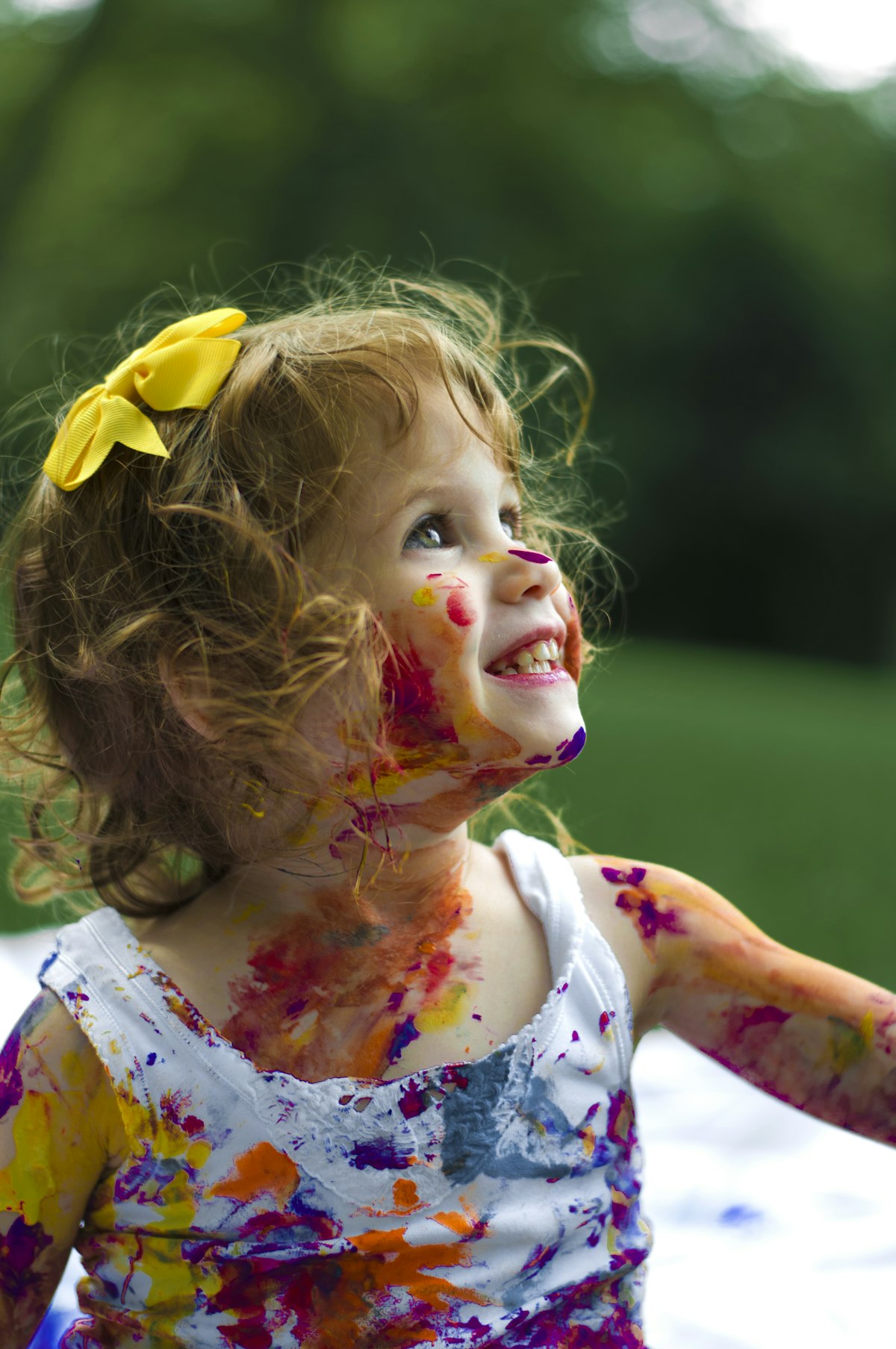 Joyful girl painted with colours, wearing a yellow bow