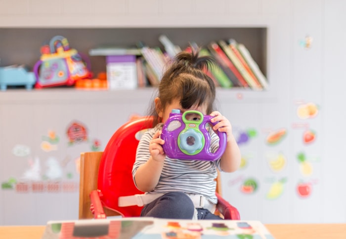 Toddler holding a toy camera in the play area